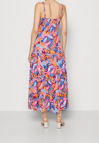 Robe maxi florale avec des teintes vives de rose, bleu et orange ; elle présente des bretelles fines, un dos smocké et une jupe en couches et fluide.