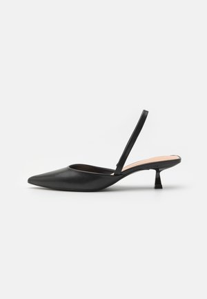 Chaussure slingback noire à bout pointu, talon kitten bas et fine bride, vue de côté sur fond blanc.