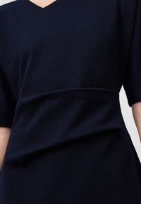 Granatowa sukienka z dekoltem w serek, krótkimi rękawami i subtelnym wzorem w prążki. Tkanina wygląda na gładką z minimalnym marszczeniem w talii.