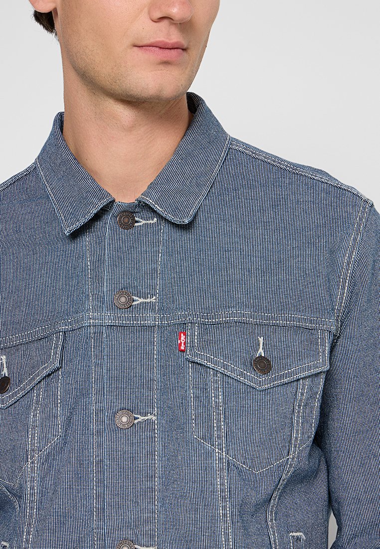 Veste en denim avec un motif rayé bleu et blanc, dotée d'un col, d'un devant boutonné et de deux poches poitrine avec des fermetures à bouton rond.