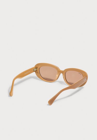 Lunettes de soleil ovales brun clair avec verres teintés assortis et branches épaisses et courbées, vues de dos sur une surface blanche.