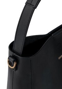 Schwarze Lederhandtasche mit glatter Oberfläche, ausgestattet mit einem langen Griff, einem goldfarbenen Hardware-Ring und minimalem Nähdetail.