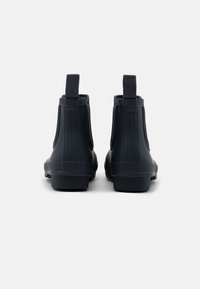 Bottes de cheville en caoutchouc noir avec texture à nervures verticales, tirettes à l'arrière et semelle plate pour un enfilage facile.