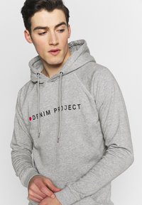 Grijze hoodie van zacht materiaal met een zwart logo "DENIM PROJECT" en een rode stip. Het heeft een capuchon met trekkoord en ribgebreide manchetten.