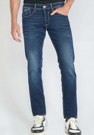 Dark blue denim jeans with a straight leg design, five pockets, and subtle fading on the front. Paired with black and white sneakers.