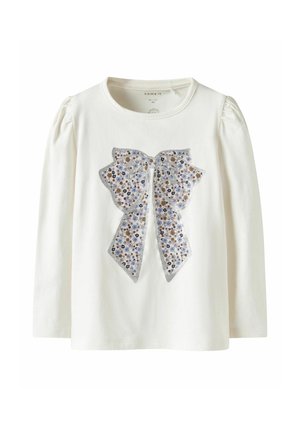 Long-sleeve white cotton shirt featuring a floral print bow in blue, orange, and silver with puffed sleeves and a round neckline.