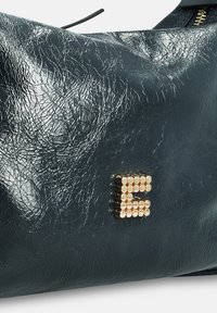 Donker groene leerachtige tas met een gerimpelde textuur en een goudkleurige kralenletter 'E' op de voorkant.