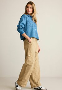 Jeans cropped jakke i lys blå med en lomme, parret med khaki brede cargo-bukser med sidelommer og sølv snap-lukninger.