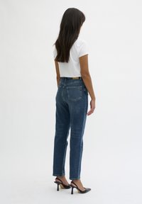 Jeans a vita alta di colore blu scuro con una vestibilità rilassata. Presentano cinque tasche e un'etichetta in pelle sulla cintura. Abbinati a una t-shirt bianca e tacchi neri.
