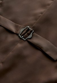 Brunt stof med en glat tekstur med en rektangulær sort metalspænde og en matchende stofrem.