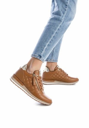 Zapatillas de cuero marrón con detalles acolchados, cremallera lateral y un acento en el talón texturizado en contraste, combinadas con denim de color azul claro.