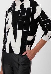 Maglione a righe in bianco e nero con lettere audaci e a contrasto, dotato di un collo alto e una vestibilità morbida. Abbinato a pantaloni in pelle nera aderenti.