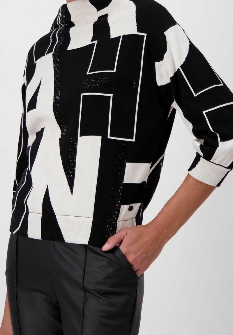 Maglione a righe in bianco e nero con lettere audaci e a contrasto, dotato di un collo alto e una vestibilità morbida. Abbinato a pantaloni in pelle nera aderenti.