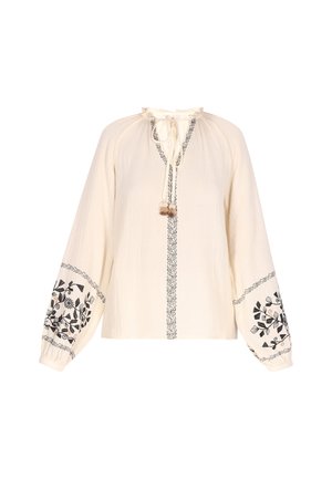 Blusa color crema con mangas largas y recogidas. Presenta bordados florales negros en las mangas y un escote con lazo y borlas. Tejido texturizado.
