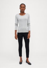 Camisola de manga longa cinza claro, com decote redondo, textura suave, combinada com calças pretas ajustadas e sapatos planos pretos. Design simples, sem padrões.