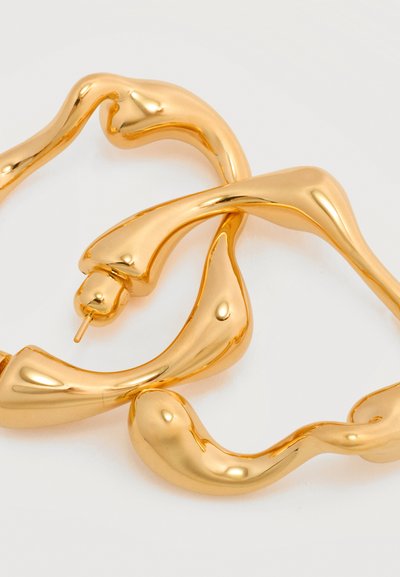 Ζεύγος ακανόνιστου σχήματος, λαμπερών χρυσών σκουλαρικιών κρίκων με ομαλή, ρευστή σχεδίαση και κλείσιμο με καρφί στο πίσω μέρος, σε λευκό φόντο.