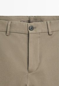 Khaki bukser lavet af tekstureret stof med en klassisk pasform, en enkelt sort knaplukning og et fladt frontdesign.