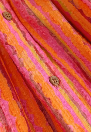 Multicolored fabric featuring wavy stripes in orange, pink, and yellow, with a wooden button detail on the right side.