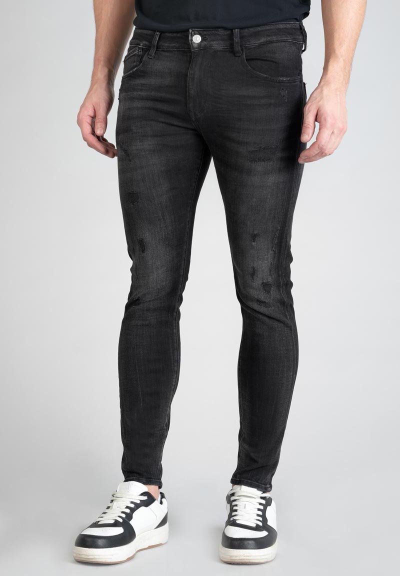 Jean en denim noir à coupe slim, présentant des détails usés et une texture lisse, associés à des baskets noires et blanches.