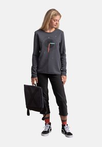 Felpa grigia a maniche lunghe con un design grafico in nero, rosso e blu. Abbinata a pantaloni neri a tre quarti e sneakers nere.