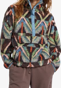 Fleece-pullover med et multicolor geometrisk mønster, der har en lys blå snap placket og en frontlomme. Blødt, struktureret stof.
