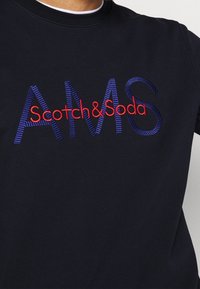 Námornická mikina s výrazným vyšívaným textem "AMS" v modré barvě a "Scotch&Soda" v červené, kulatým výstřihem, hladkým materiálem a uvolněným střihem.