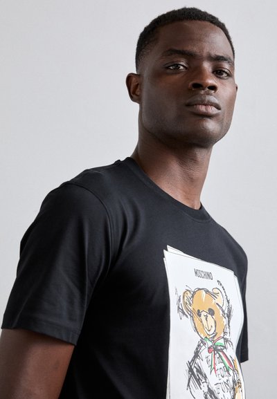 T-shirt en coton noir avec un motif d'ours coloré et un logo au-dessus. Manches courtes, col rond, texture lisse.