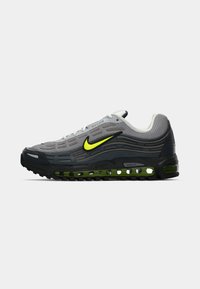 Nike Air Max sneaks pelēkā sietā ar melnā un zaļā gumijas detaļām. Iezīmēta ar izteiktu dzeltenu swoosh un Max Air amortizāciju.