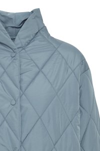 Šviesiai mėlynas quilted švarkas su aukštu apykakle ir dviem apvaliais mygtukais. Medžiaga turi lygią tekstūrą su diamanto raštais.
