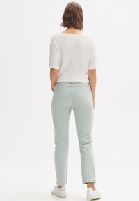 Top corto bianco a maniche corte con texture abbinato a pantaloni slim-fit verde chiaro. L'outfit è completato da sneakers bianche.