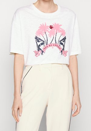 Biała krótka koszulka z różowymi palmami, czarnymi sylwetkami na rolkach i różowym banerem "See By Chloe", noszona z kremowymi spodniami.
