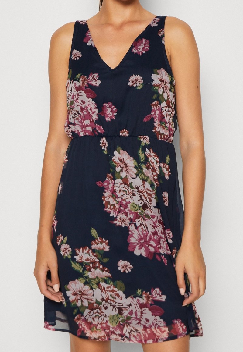 Ärmlös blommig klänning med djup V-ringning, marinblå bakgrund och stora rosa och gröna blommönster. Lätt, flödande tyg.