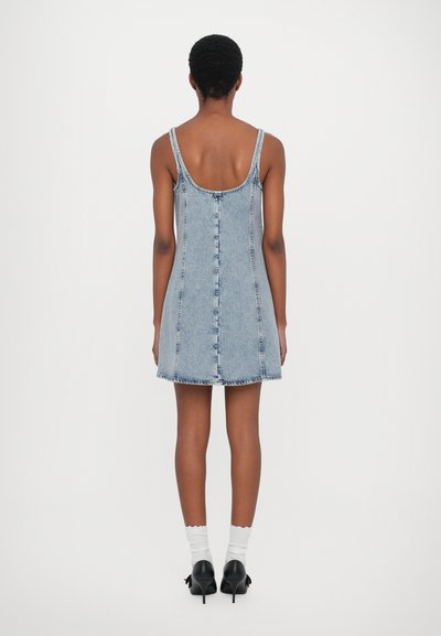 Denim dress, light blue, sleeveless with a scoop back, features a button-down front and frayed hem. Worn with white socks and black heels.