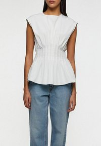 Hvid peplum top med korte ærmer, der har lodrette plisseringer og et tætsiddende liv, parret med lyseblå, løsthængende jeans.