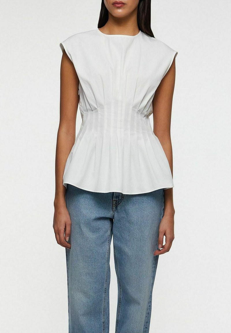 Vitt peplumtop med kort ärm, med vertikala veck och en figurnära bodice, kombinerat med ljusblå, löst sittande jeans.