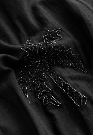 Czarna tkanina z misternym czarnym haftem w wzór liści, w towarzystwie małych koralikowych akcentów. Miękka i teksturowana powierzchnia.