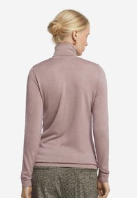 Ljusrosa långärmad polotröja med mjuk textur, figurnära passform och ribbad mudd, kombinerad med en mönstrad grå kjol.