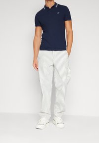 Námořnická polo tričko s kontrastním bílým límcem, spárované s bílými pruhovanými kalhotami a bílými teniskami, s uvolněným a pohodlným střihem.