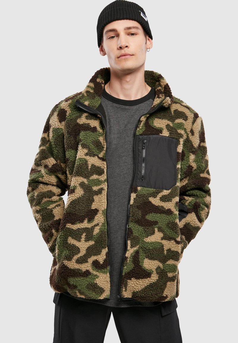 Karvane, roheka, pruuni ja beežika kamuflaažimustriga jakk, millel on lukuga must rindatasku ja püstkrae. Kandmisel on selle all tumedat halli särki.