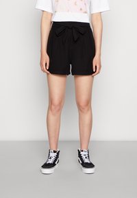 Schwarze Shorts aus leichtem Stoff mit einem gebundenen Gürtel in der Taille. Kombiniert mit schwarz-weißen High-Top-Sneakern.