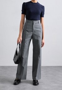 Top de punto acanalado en azul marino con mangas cortas, combinado con pantalones de pierna ancha grises de cintura alta. Un elegante bolso negro y unos mocasines negros completan el look.