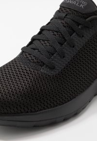 Sort net sneakers med en tekstureret overdel, flade snørebånd og en polstret sål, designet til åndbarhed og komfort.