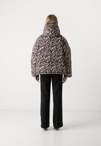 Chaqueta acolchada de estampado de leopardo con capucha, con un corte holgado y mangas anchas, combinada con pantalones negros rectos.