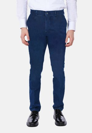 Pantaloni slim-fit blu scuro realizzati in un tessuto testurizzato, dotati di una chiusura con un singolo bottone frontale e tasche standard, abbinati a scarpe nere.