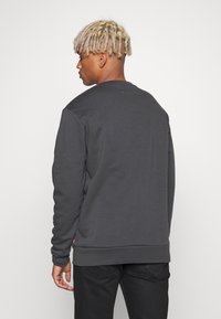 Sudadera gris oscura de manga larga, con diseño de cuello redondo y puños acanalados. Presenta un pequeño logo cerca del dobladillo. Textura suave.