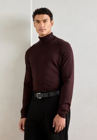 Bordeaux turtleneck sweater van een zachte brei, gedragen met een zwarte riem en donkere broek, met een slim fit en lange mouwen.