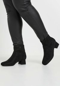 Botines de ante negros con puntera redondeada, tacón cuadrado y detalle de cremallera lateral. Textura suave y acabado blando.