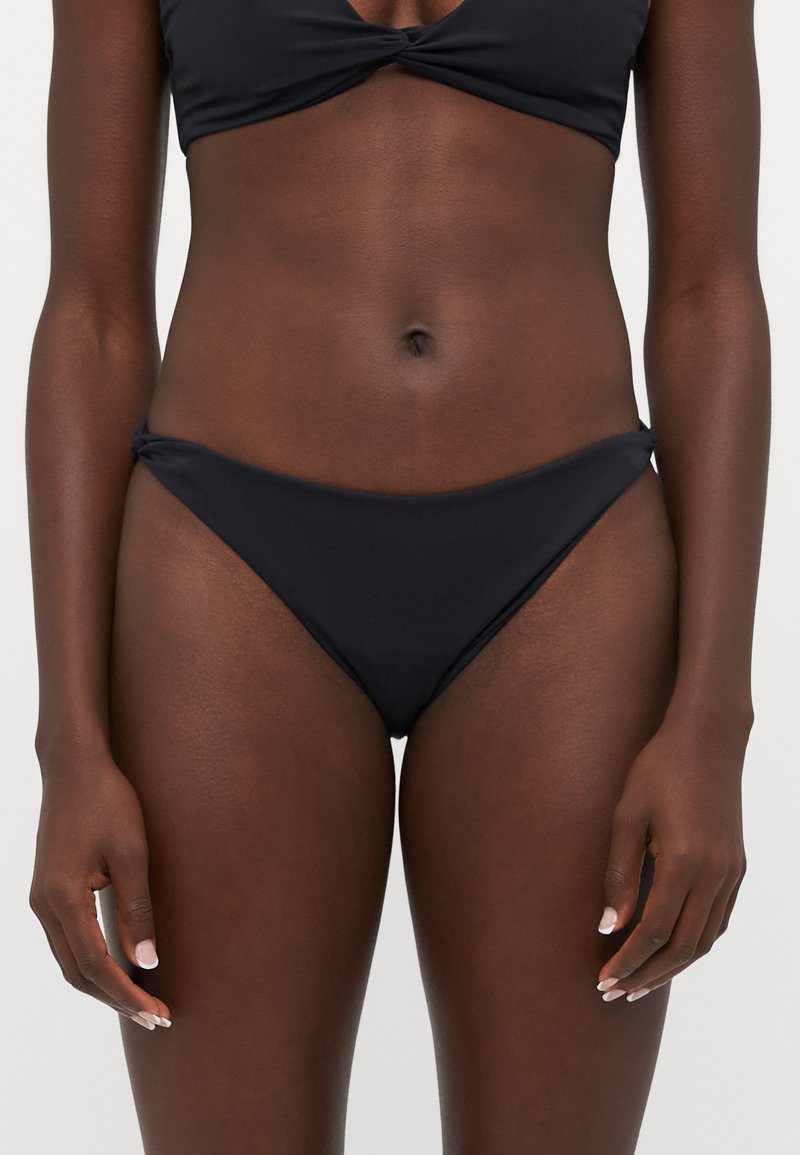 Top del bikini nero con design a nodo attorcigliato, abbinato a slip bikini a vita bassa coordinati. Tessuto morbido e elasticizzato. Stile minimalista.