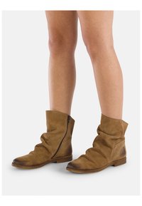 Stivaletti alla caviglia in suede marrone con un design morbido, zip laterale, suola piatta e punta leggermente arrotondata. Presentano una lieve variazione di colore sulla punta.