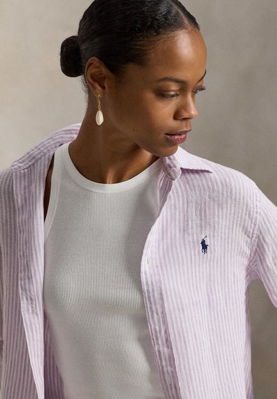 Πουκάμισο με κουμπιά σε ανοιχτό μωβ και λευκές ρίγες, φορεμένο πάνω από λευκή ριμπ μπλουζάκι χωρίς μανίκια, με μικρό μπλε λογότυπο στο αριστερό στήθος.